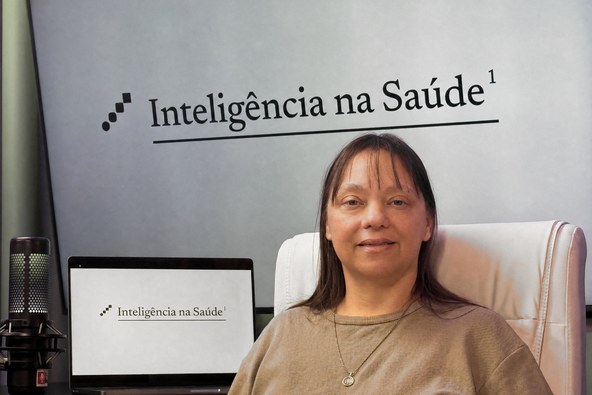 Cassiana Meyer no estúdio do Inteligência na Saúde, com o nome do projeto na parede ao fundo.